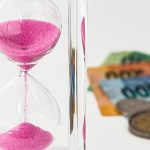Hour glass with pink sand and money - coins and notes blurred n the the background