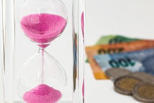 Hour glass with pink sand and money - coins and notes blurred n the the background